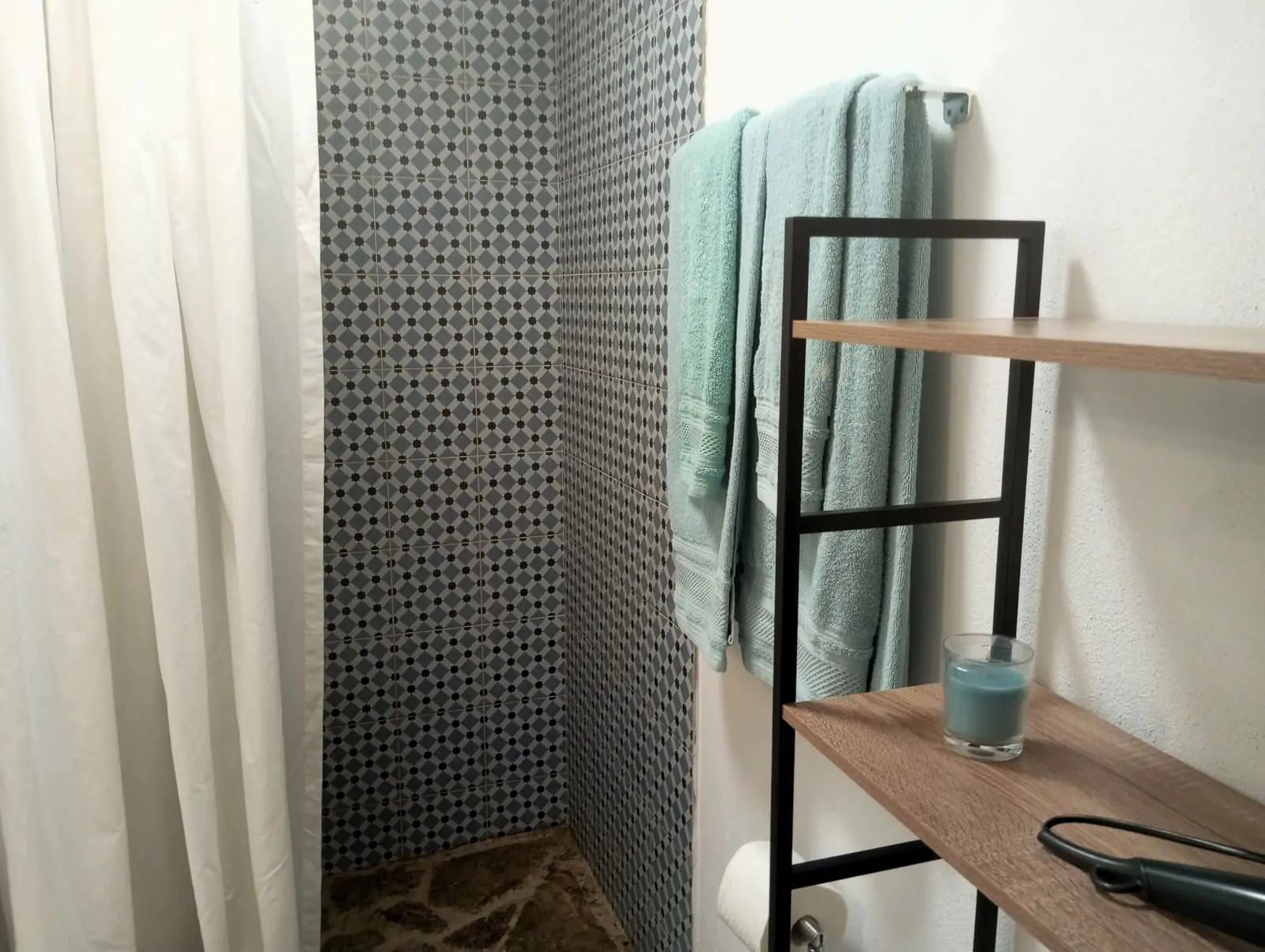 Casa de banho com azulejo padronado e toalhas verde-azuladas