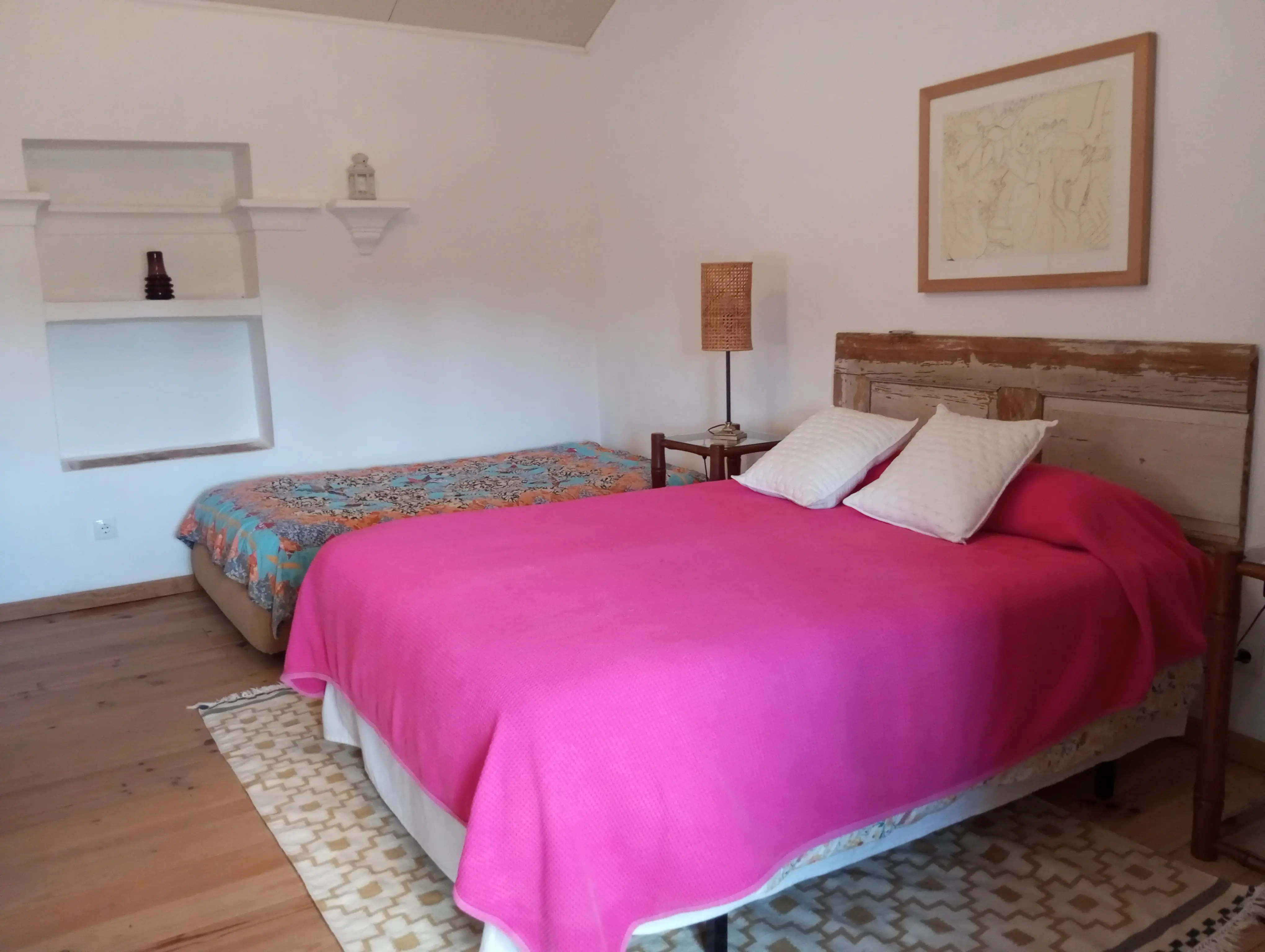 Quarto luminoso com colcha rosa viva e cabeceira de madeira