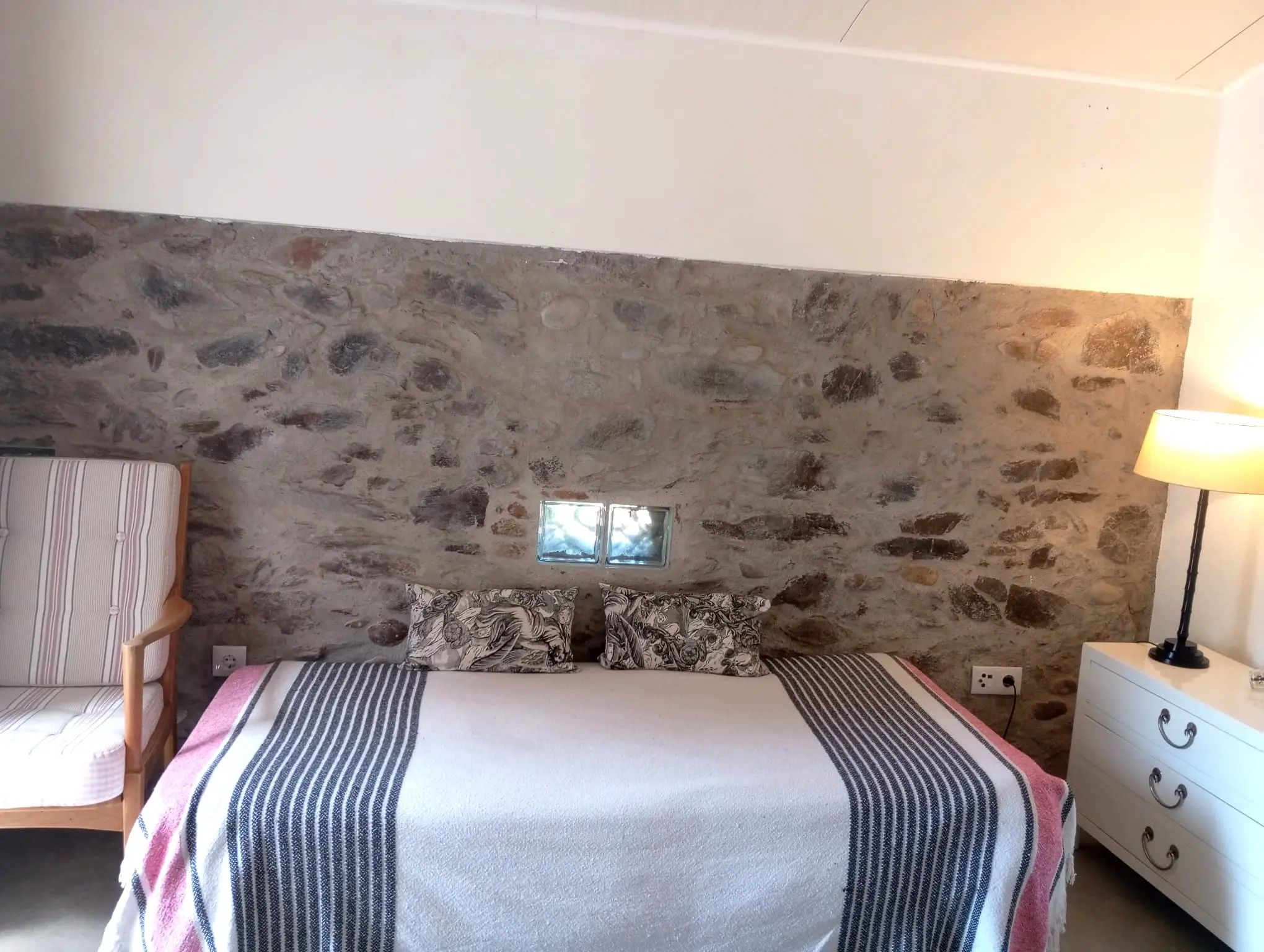 Quarto rústico com cabeceira em parede de pedra e manta de riscas