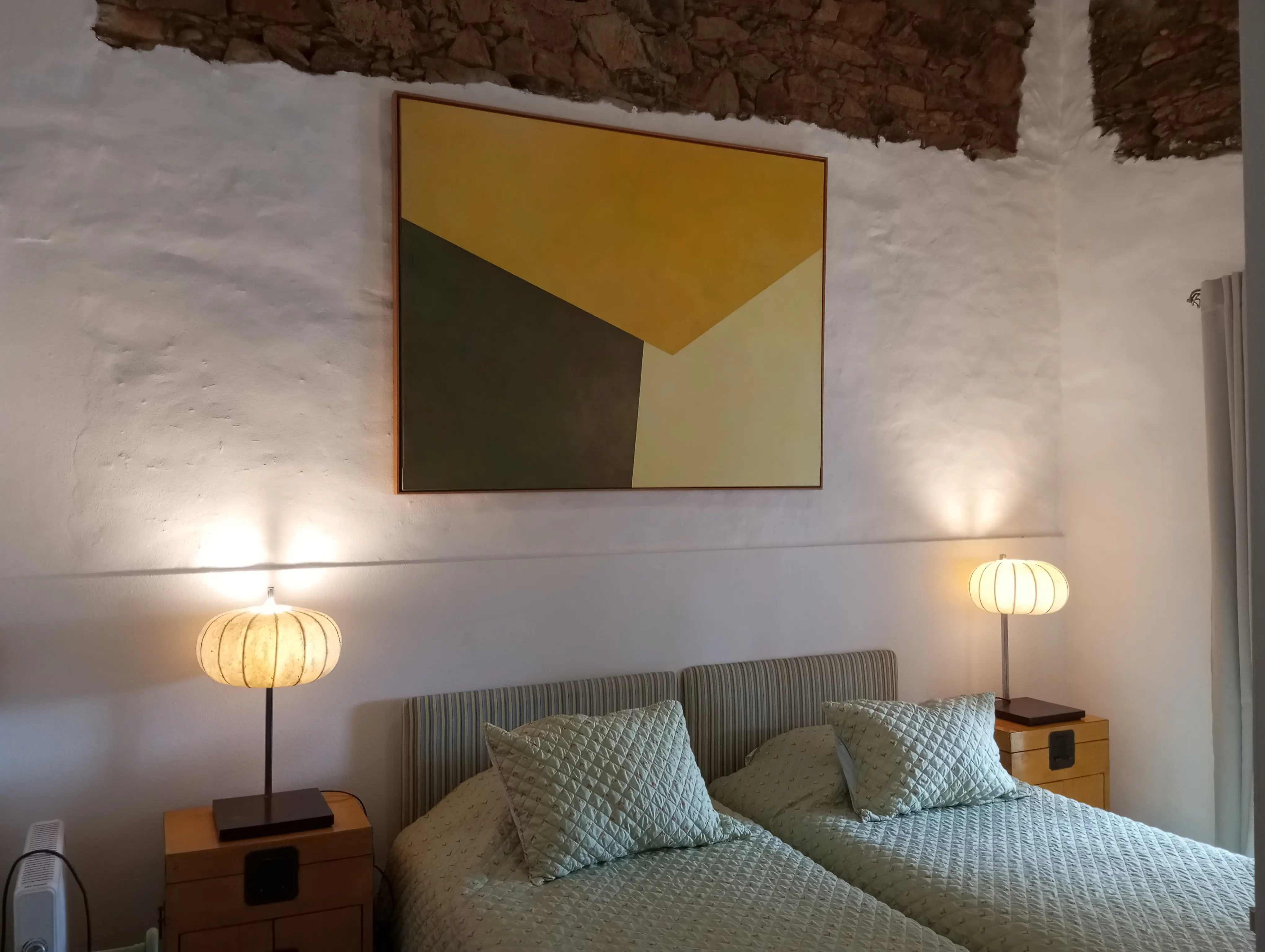 Quarto com duas camas, arte em verde e amarelo e candeeiros a condizer