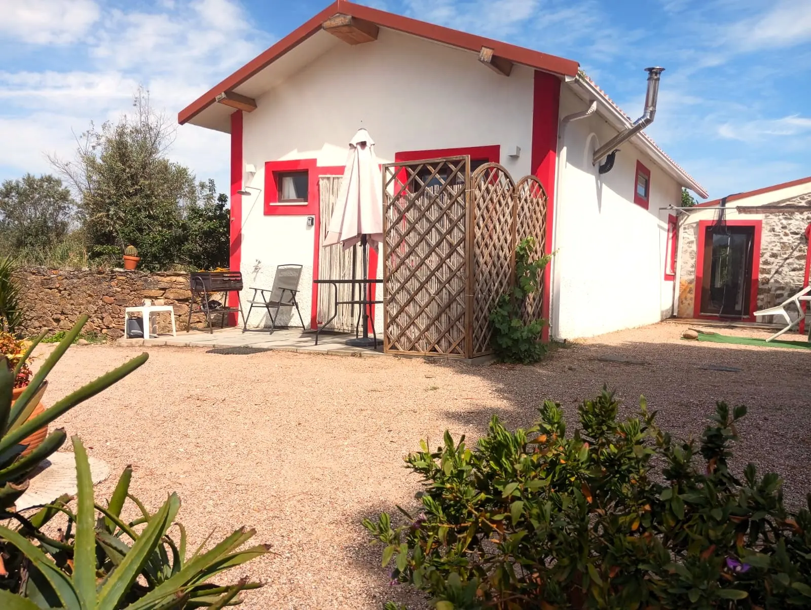Exterior da Casa Pequena, branca com remates vermelhos, com mesa e chapéu de sol à entrada