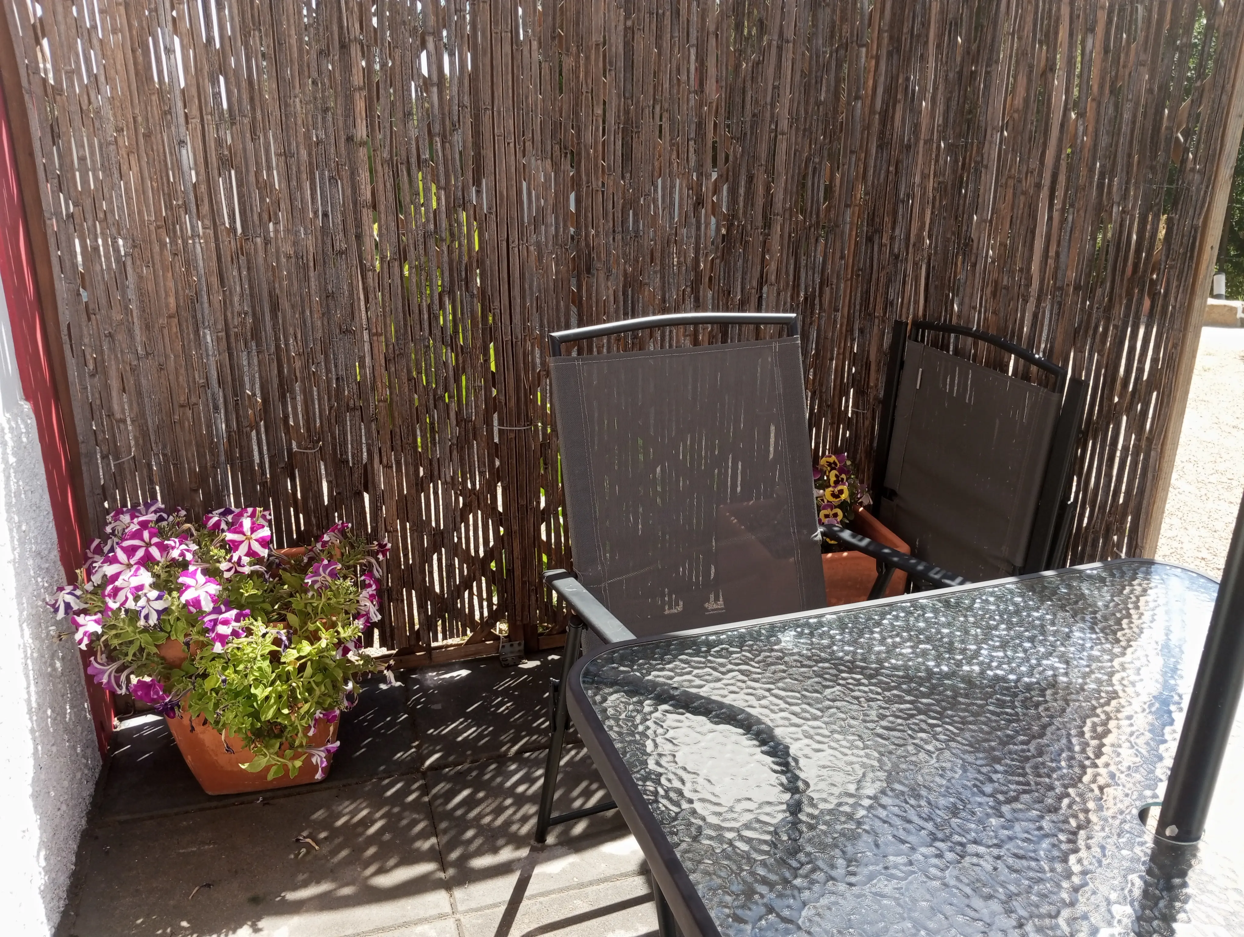 Terraço à entrada da Casa Pequena, com mesa de vidro, cadeiras e vasos de flores