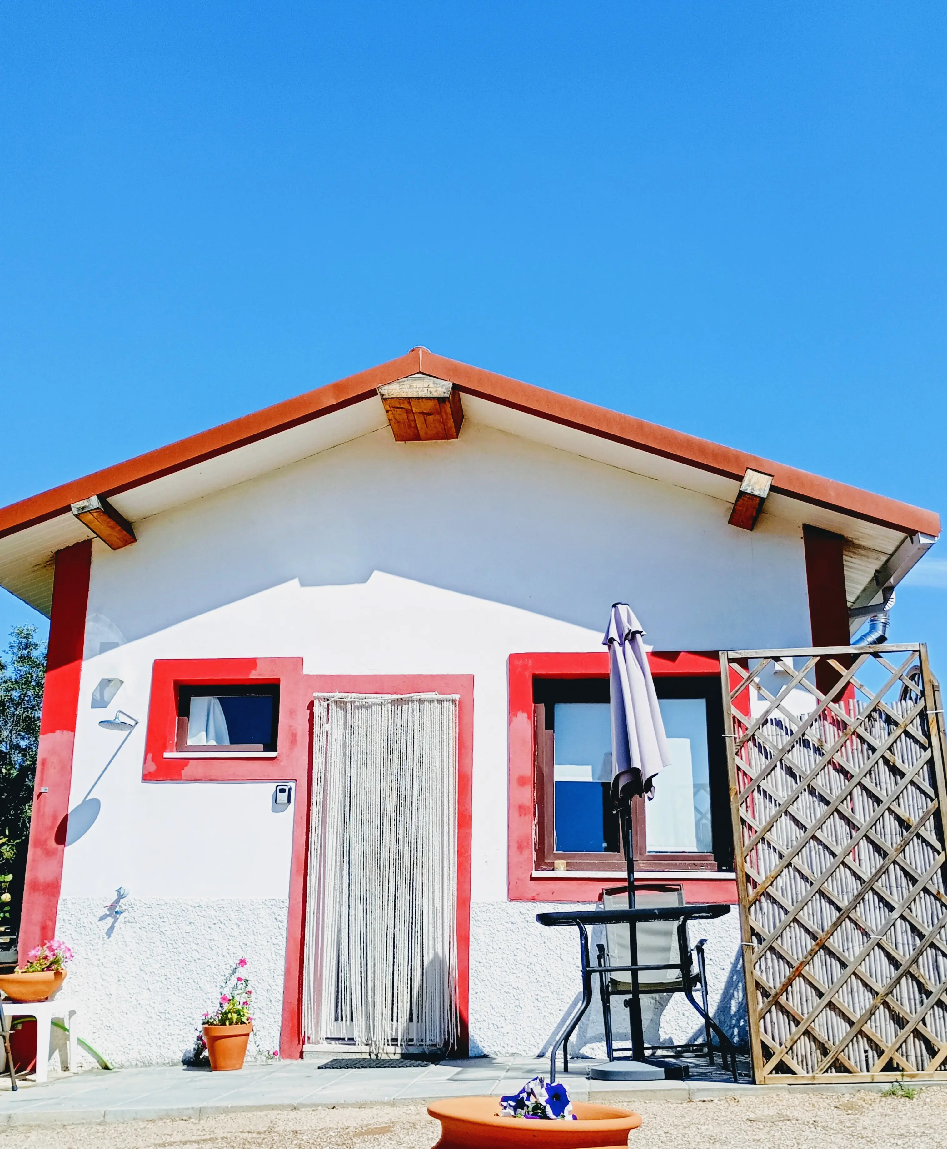 Fachada da Casa Pequena, branca com remates vermelhos, chapéu de sol e mesa à entrada
