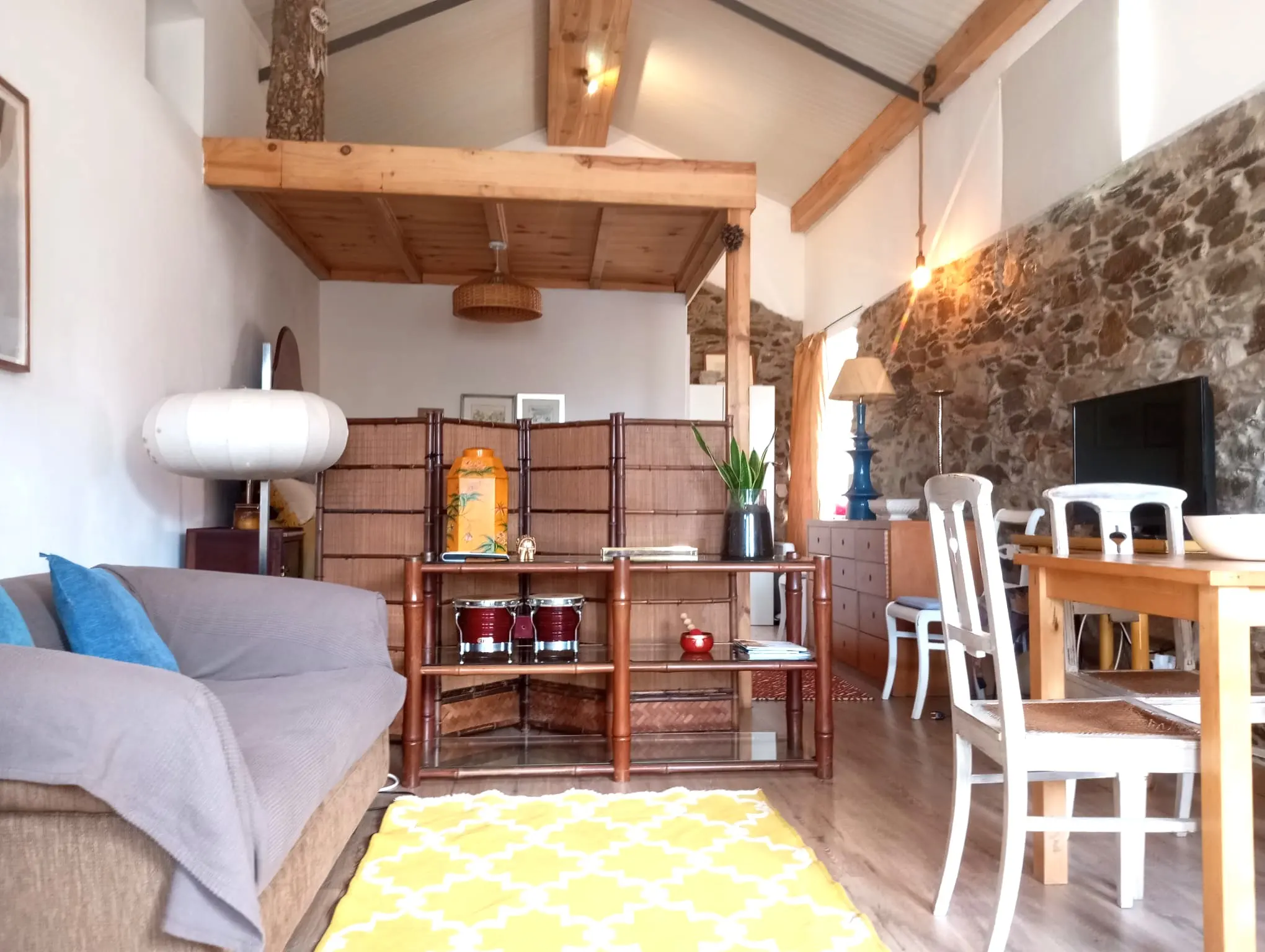 Sala ampla com parede de pedra, vigas e tapete bohemian